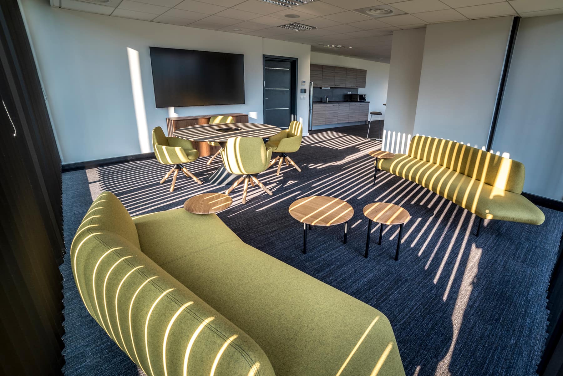 L'espace détente de la salle, canapés et tables basses, écran mural et kitchenette en fond