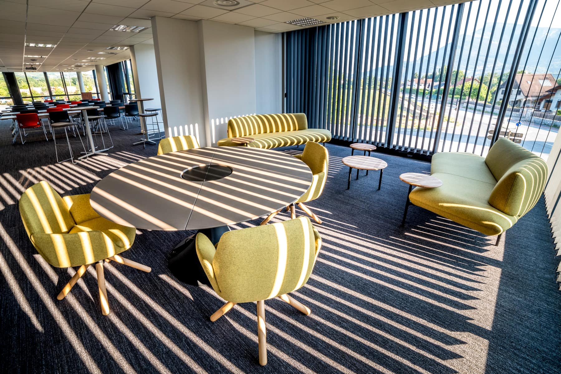 L'espace détente de la salle, table ronde et fauteuils verts devant les baies vitrées